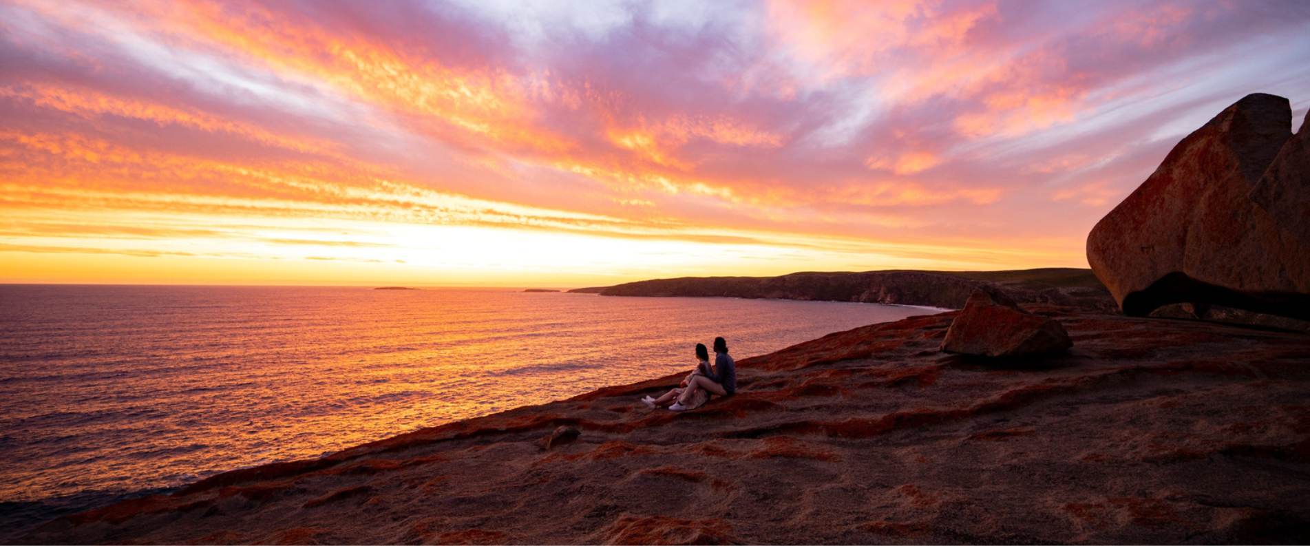 Two people watching the glowing purple and yellow sunset over Remarkable Rocks on kangaroo island